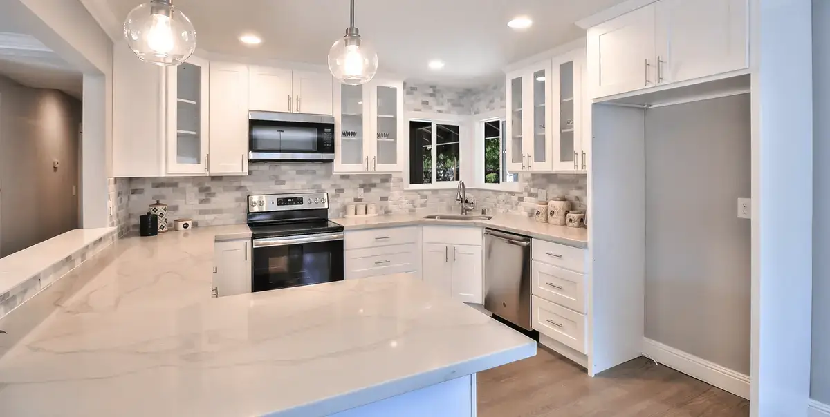 Bright and modern kitchen with white cabinets, sleek countertops, stainless steel appliances, and a neutral backsplash. The open layout creates a welcoming space for cooking and entertaining. Ready to upgrade your kitchen? Start planning your remodel today!