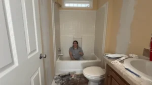 A woman sitting in a bathtub surrounded by remodeling tools and supplies during a bathroom renovation project. Get help estimating your small bathroom remodel costs today!