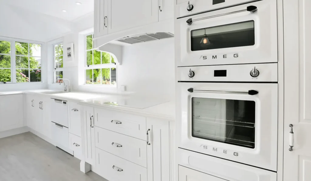 Bright white kitchen with modern appliances and large windows. Click here to learn how to remodel your small kitchen to maximize space and light.