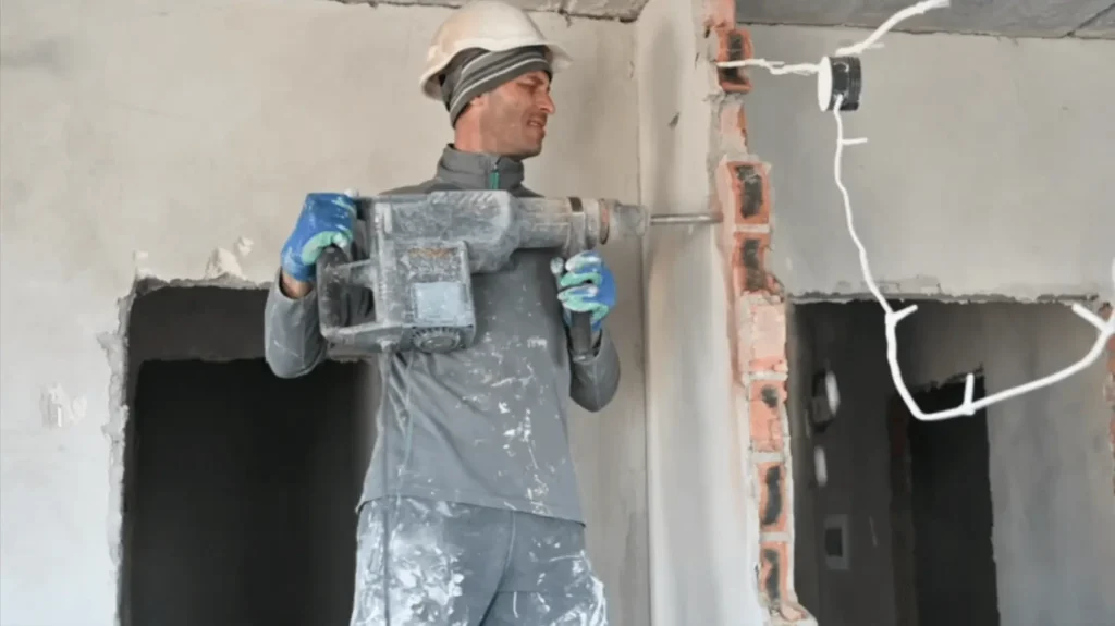 Construction worker demolishing a wall with a heavy-duty drill. Hire a contractor for your renovation project to ensure professional results.