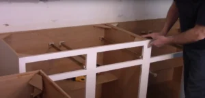 A person carefully measuring and aligning a wooden cabinet frame for replacement, demonstrating how to install new cabinets without disturbing the existing countertop.